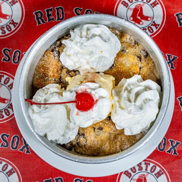 Matty G's warm cookie skillet dessert with ice cream, whipped cream, and a cherry on a Red Sox tablecloth.