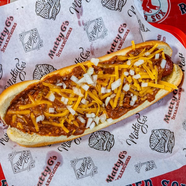 A Matty G's chili cheese dog with diced onions on branded paper in a red basket.