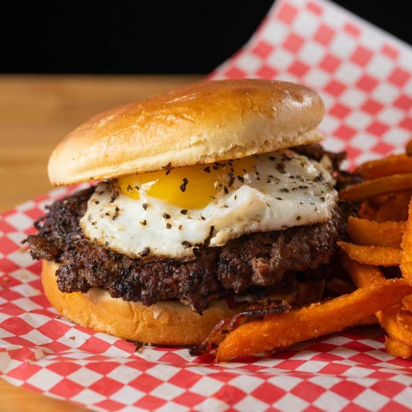 Matty G's Steakburger with a fried egg and sweet potato fries on red checkered paper.