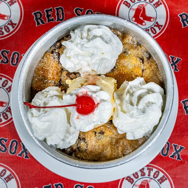 A Matty G's cookie skillet with ice cream, whipped cream, and a cherry on a Red Sox tablecloth.