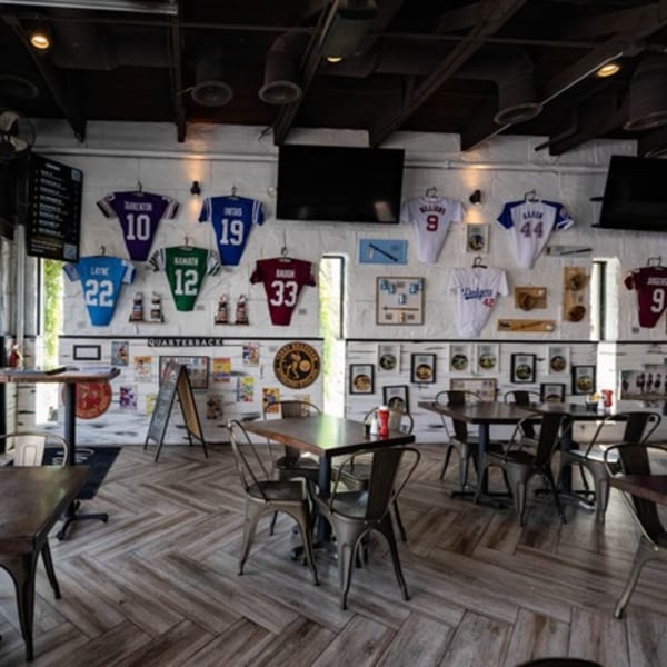 Interior of Matty G's Steakburgers with sports jerseys and memorabilia on white brick walls, and dark tables.