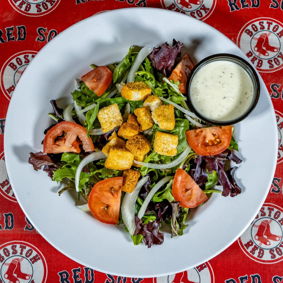 Side salad with mixed greens, tomatoes, onions, croutons, and ranch dressing on a white plate.