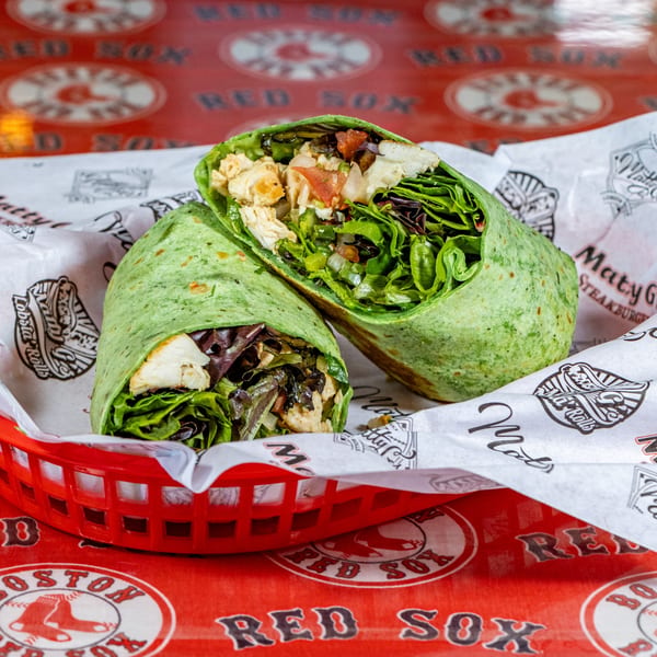 Two halves of a green tortilla wrap filled with chicken, lettuce, and vegetables in a red basket.