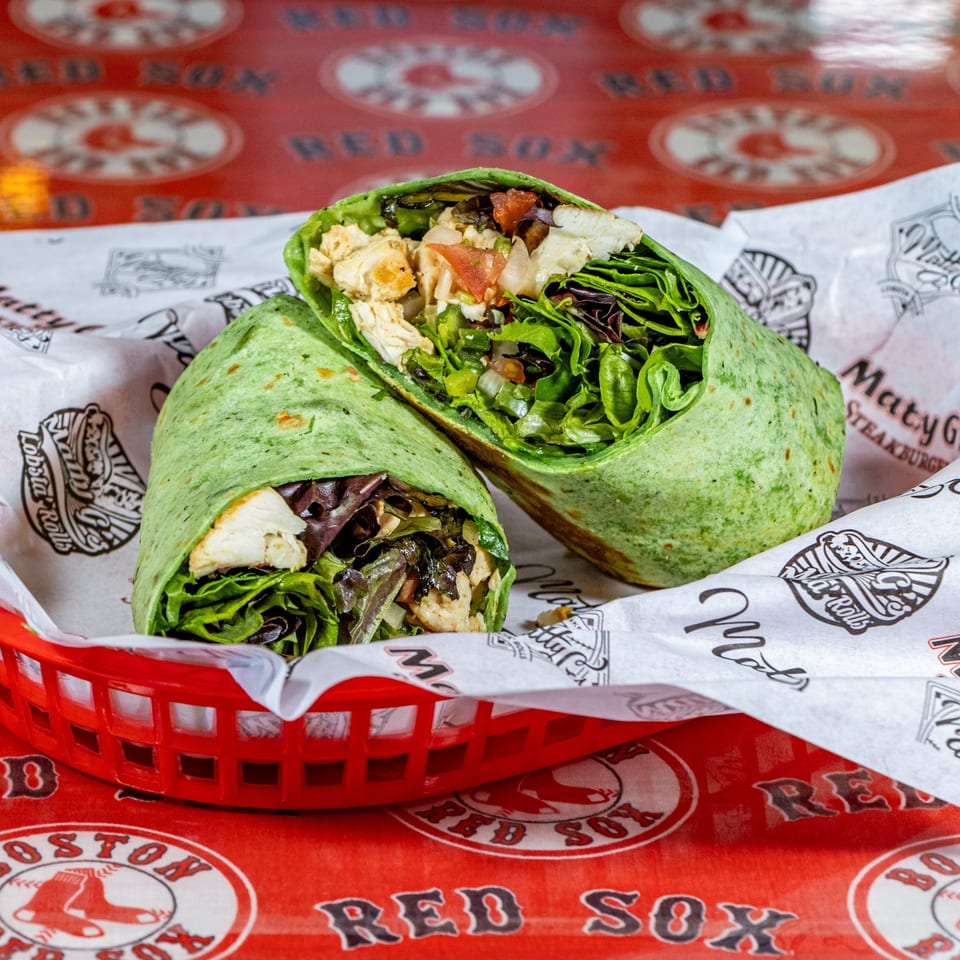 Two halves of a green tortilla wrap filled with chicken, lettuce, and vegetables in a red basket.