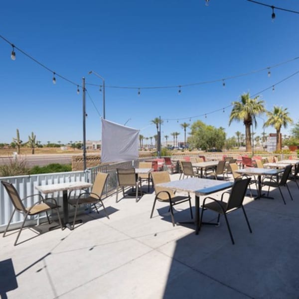 Outdoor patio with tables and chairs under string lights, palm trees and desert landscape in background.