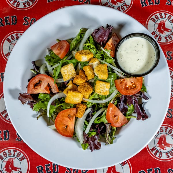 A fresh side salad with mixed greens, tomatoes, onions, croutons, and ranch dressing on a white plate.