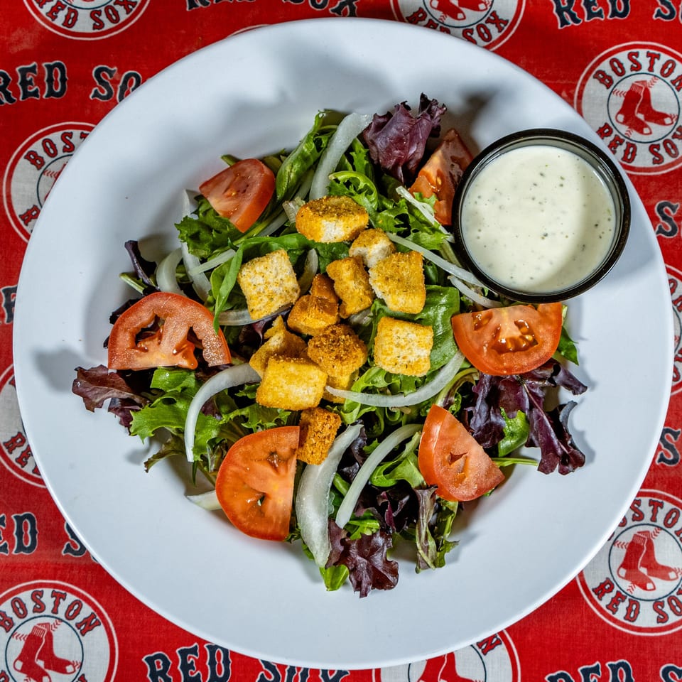 A fresh side salad with mixed greens, tomatoes, onions, croutons, and ranch dressing on a white plate.