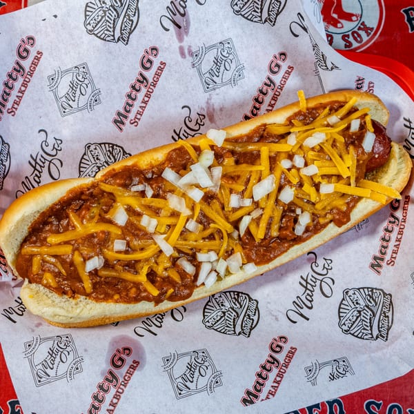 A Matty G's chili cheese dog with diced onions on branded wax paper.