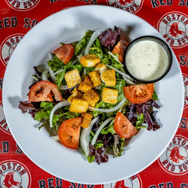 A fresh side salad with lettuce, tomatoes, onions, croutons, and ranch dressing on a white plate.