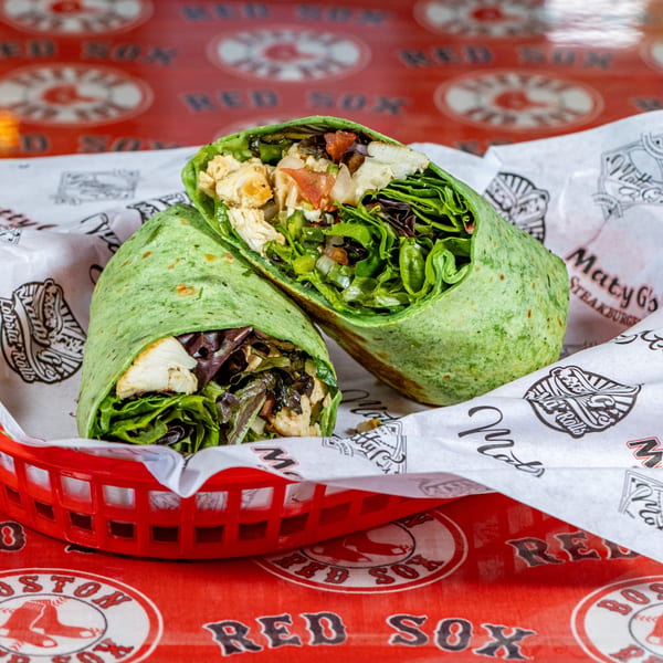 Two Matty G's chicken wraps, filled with greens and chicken, in a red basket on a Red Sox tablecloth.