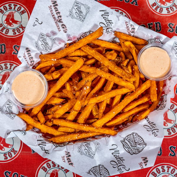 A basket of Matty G's Steakburgers fries with two dipping sauces on a Boston Red Sox tablecloth.