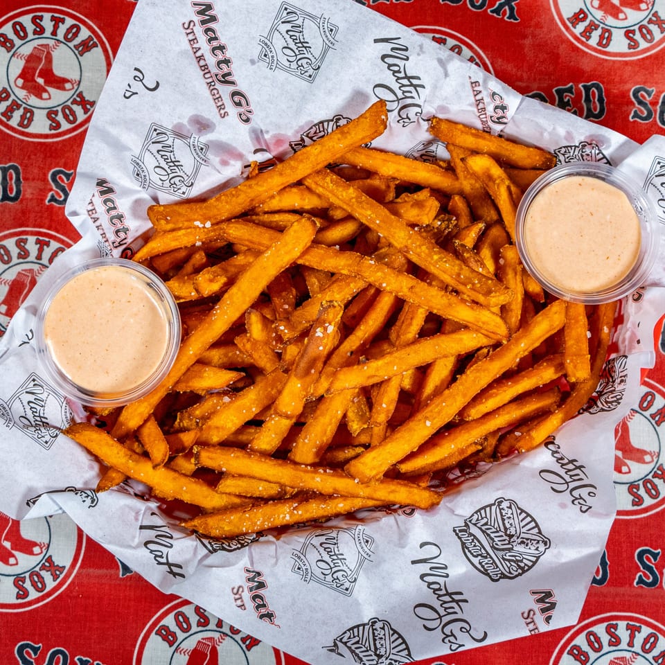 A basket of Matty G's Steakburgers fries with two dipping sauces on a Boston Red Sox tablecloth.