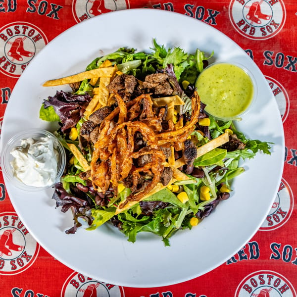 Matty G's Steakburger salad with steak, fried onions, corn, black beans, and dressings on a Red Sox tablecloth.
