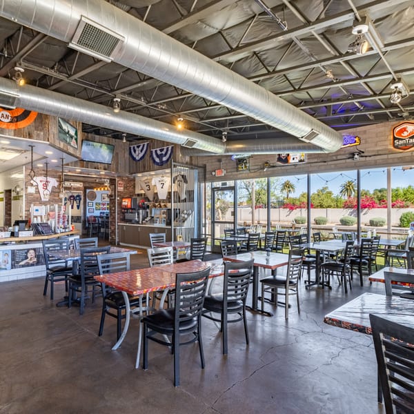 Interior of Matty G's Steakburgers, featuring dining tables, exposed ductwork, and large windows overlooking a patio.