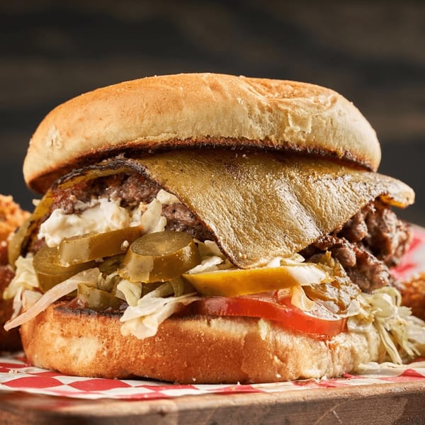 A close-up of a Matty G's Steakburger with melted cheese, pickles, and fresh vegetables.