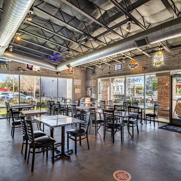 Interior of Matty G's Steakburgers, featuring empty tables, chairs, and large windows with street views.