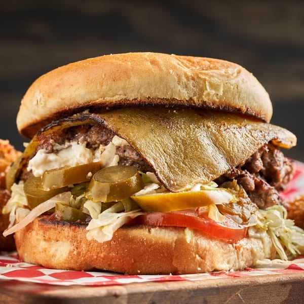 Close-up of a Matty G's Steakburger with melted cheese, pickles, tomatoes, and shredded lettuce.