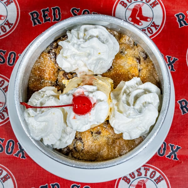 Warm chocolate chip cookie skillet topped with vanilla ice cream, whipped cream, and a cherry.