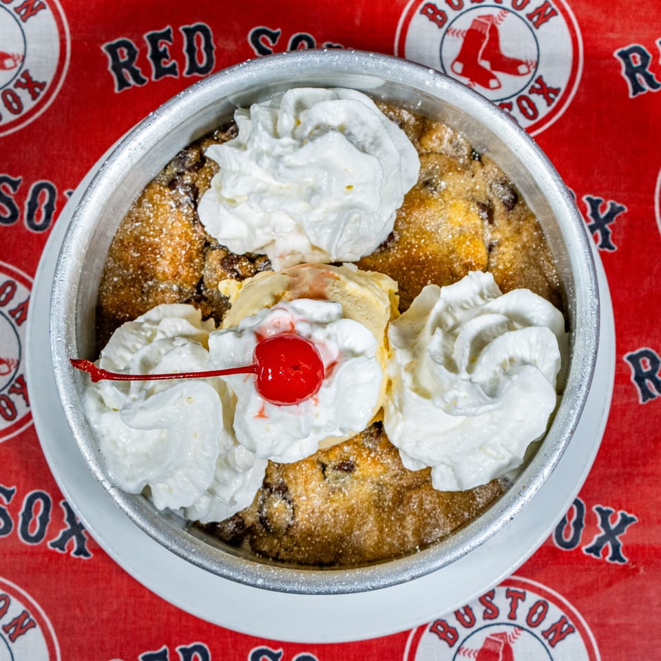 Warm chocolate chip cookie skillet topped with vanilla ice cream, whipped cream, and a cherry.