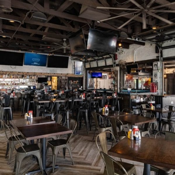 Interior of Matty G's Steakburgers with dark wooden tables, metal chairs, and a bar area.