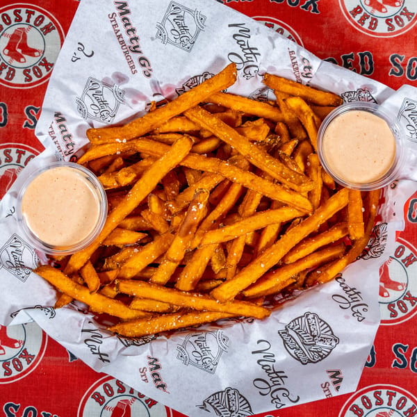 A basket of Matty G's golden-brown french fries with two dipping sauces on a Boston Red Sox tablecloth.