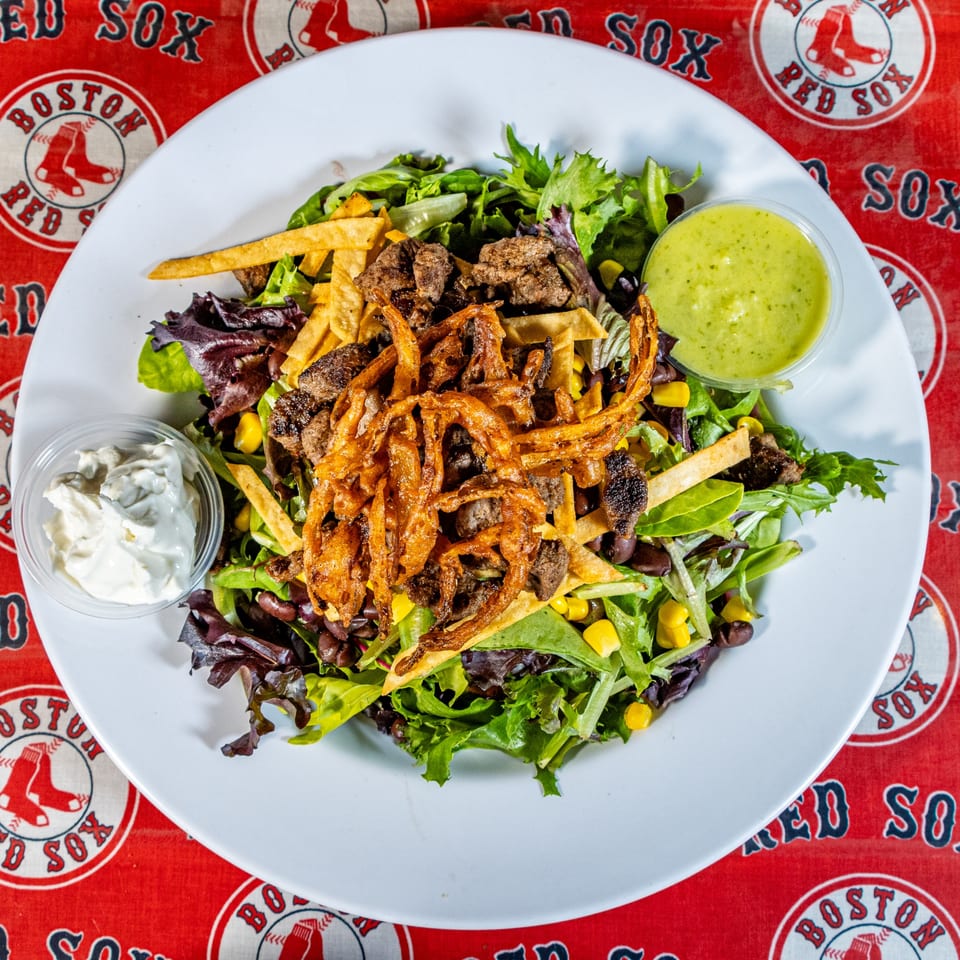 Matty G's Steakburgers salad with steak, fried onions, corn, and beans on a Boston Red Sox tablecloth.